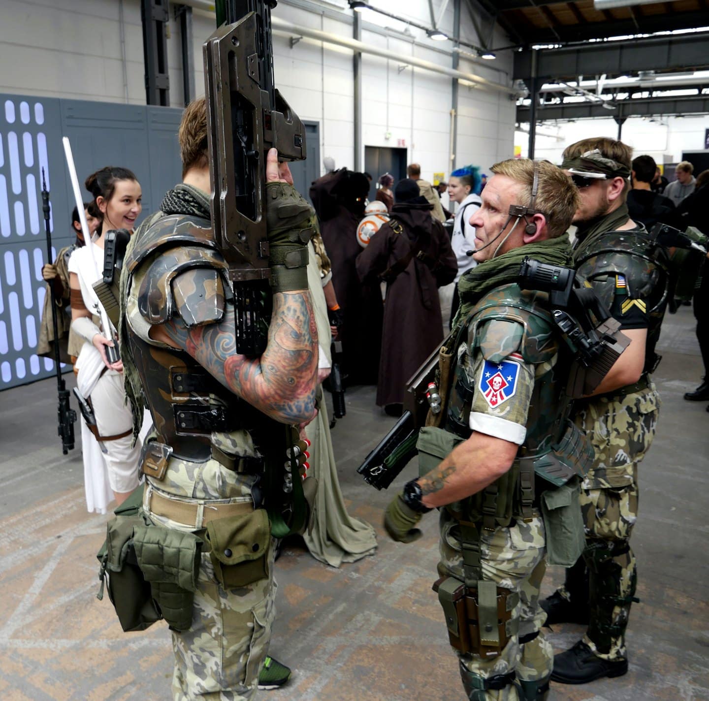 Cosplayer in tenuta futuristica che interagiscono in un affollato padiglione fieristico.